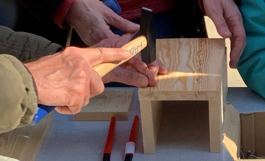 Foto die de bouw van een nestkastje met eenvoudig gereedschap (houten planken, spijkers en een hamer) illustreert
